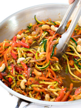 this zucchini noodle stir fry with cashews in a metal skillet with metal tongs tossing the noodles in the sauce | chefsavvy.com