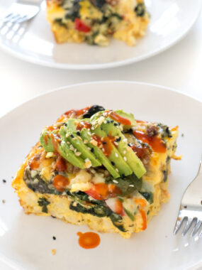 slice of breakfast casserole topped with sliced avocado on white plate