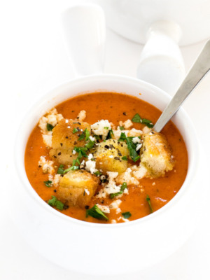 Creamy Roasted Red Pepper and Tomato Soup in a white bowl garnished with croutons, parsley, and feta cheese | chefsavvy.com