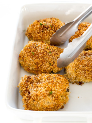 crispy oven fried chicken in a white baking dish with metal tongs