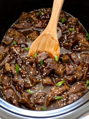 an overhead view of this slow cooker Korean beef in a crock pot with a wooden spoon garnished with sesame seeds and sliced green onions