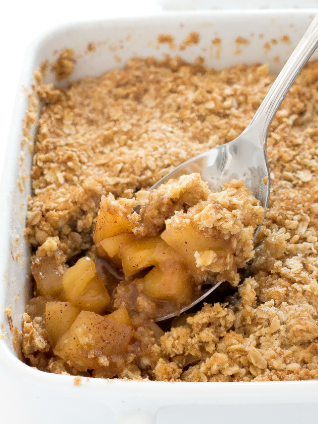 spooning apple crisp out of a white casserole dish