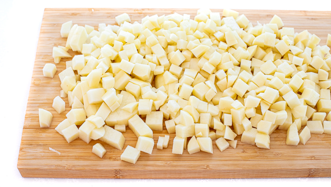 Raw potatoes after being diced, on a wooden cutting board.
