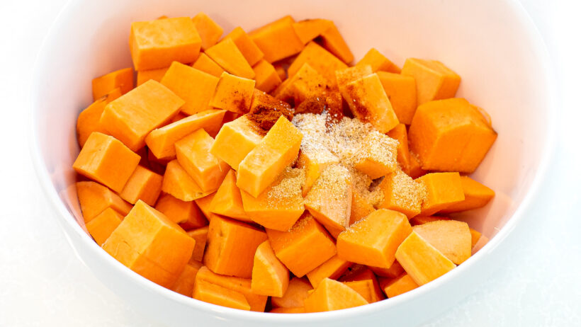 Spices and diced sweet potatoes in a mixing bowl.
