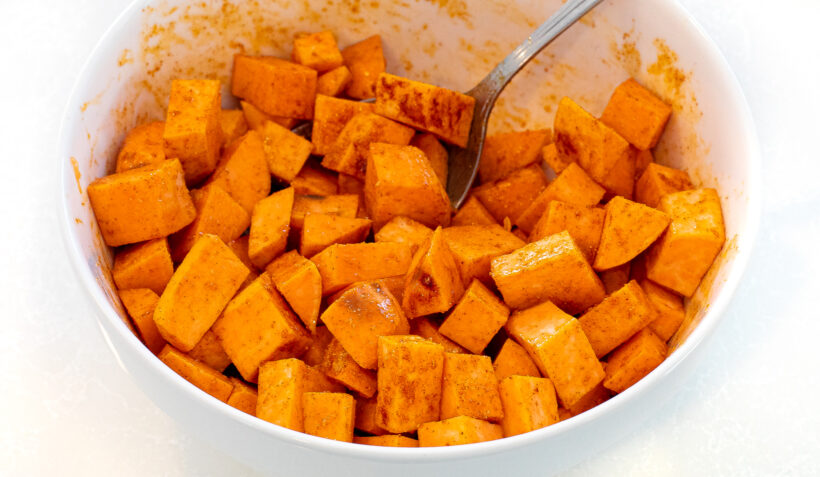 Cubes of sweet potato in a mixing bowl with spices on them.