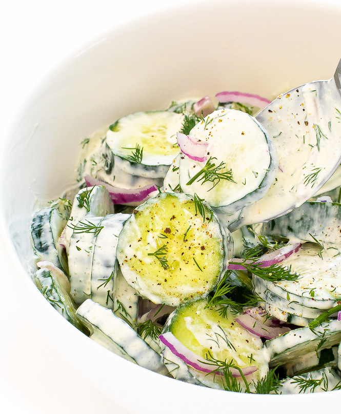 Cucumbers in a creamy dressing in a white bowl with a silver spoon.