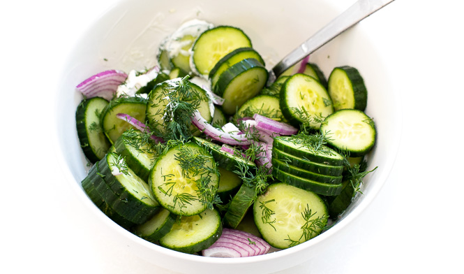Cucumbers, onion and dill in a creamy dressing in a white bowl. 