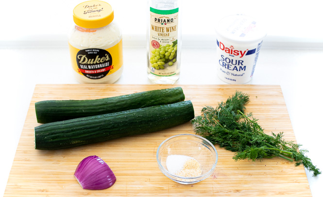 Ingredients needed for creamy dill cucumber salad on a cutting board. 