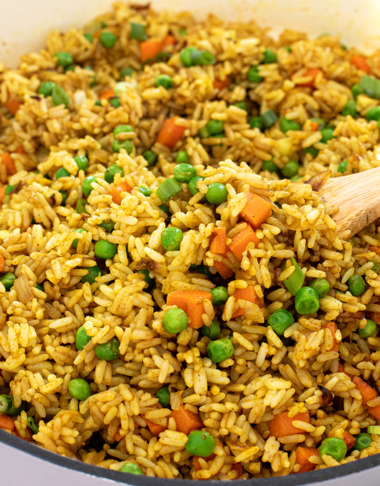 Fried rice in a skillet with a wooden spoon scooping a portion out. 