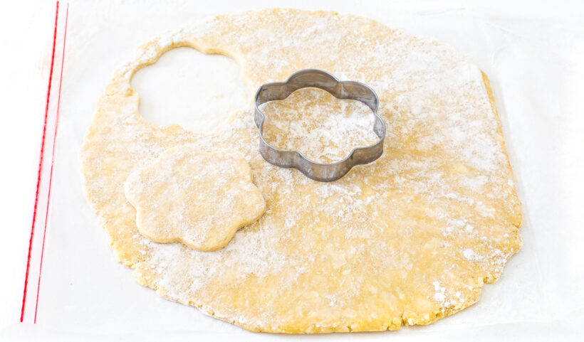 Pie dough being cut out with a flower cookie cutter.