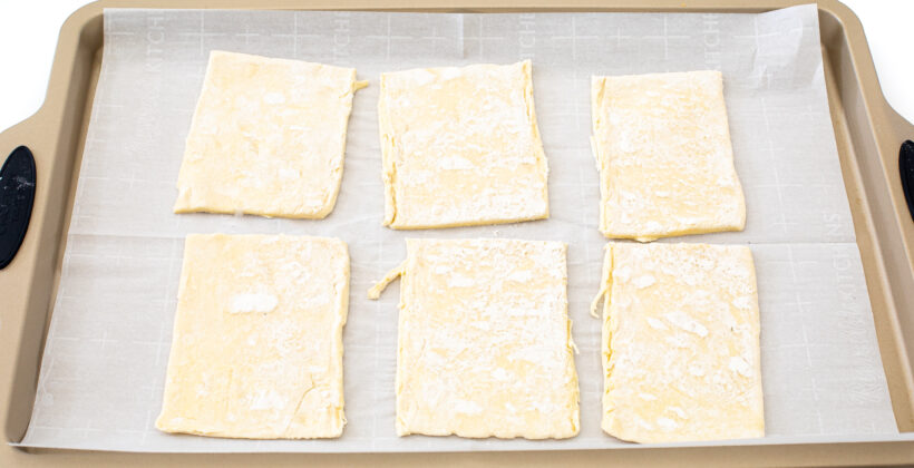 Six squares of puff pastry on a parchment lined baking sheet. 