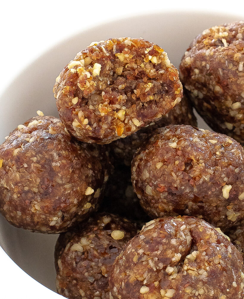 Up close shot of energy ball with a bite taken out of it on top of more balls in a white bowl.