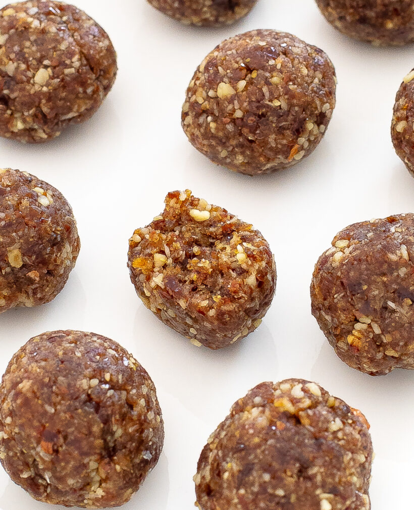 One energy bite with a bite taken out of it, surrounded by more balls on a white plate.