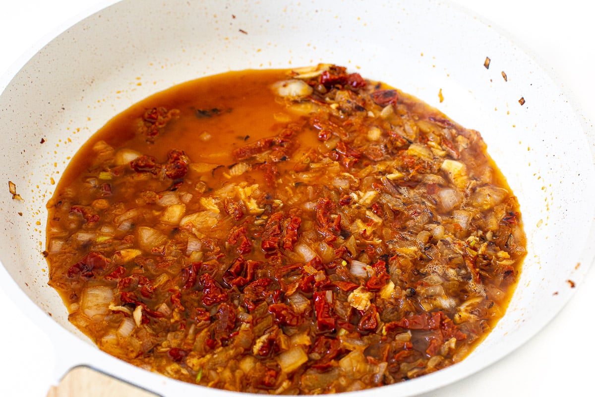 adding broth to large skillet with sun dried tomatoes for marry me chicken