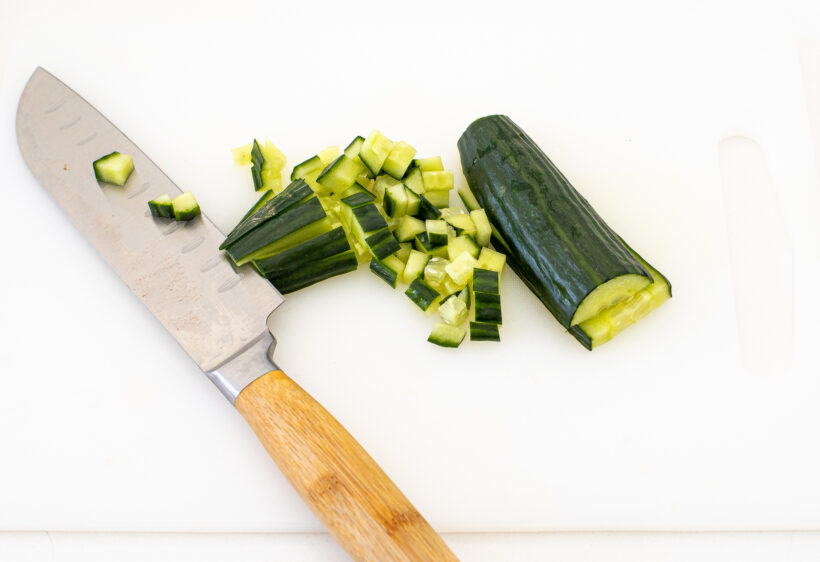 Cucumber being chopped with a chef's knife on a cutting board. 
