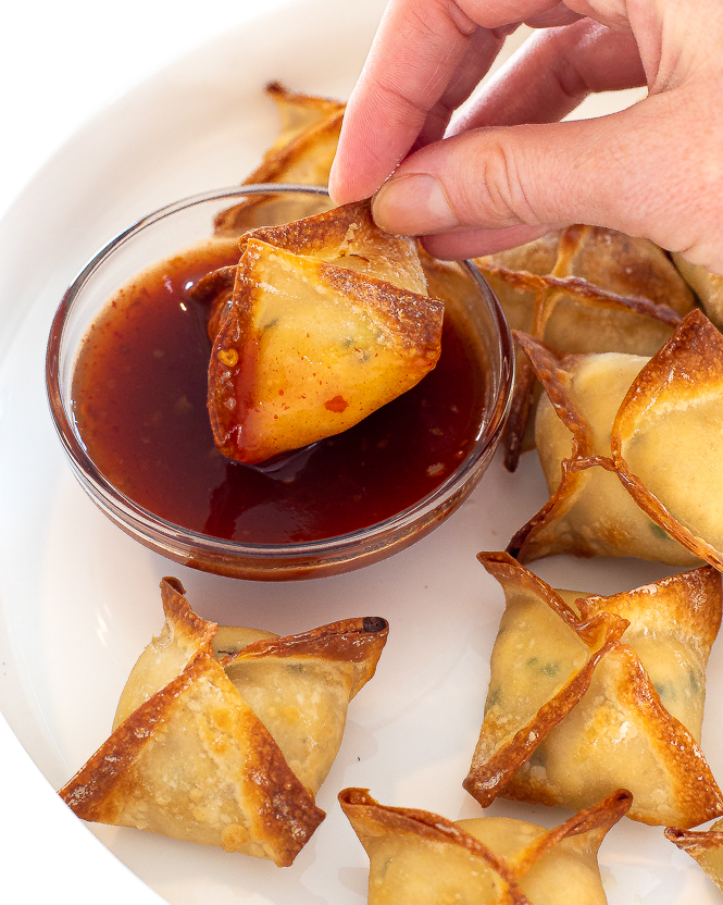 Hand dipping air fryer crab rangoon into a sauce. 