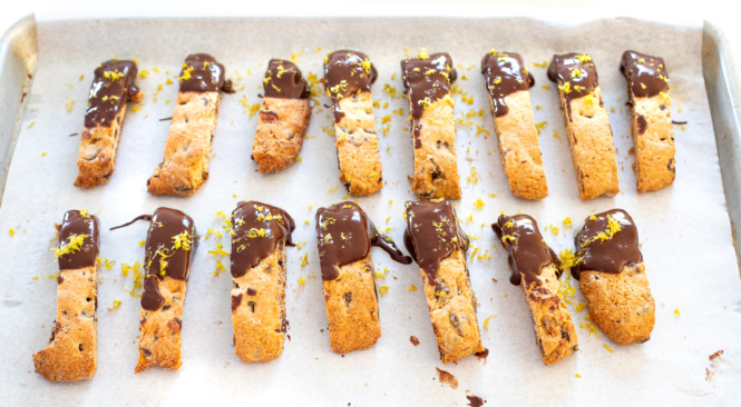 orange biscotti dipped in melted chocolate and topped with orange zest and chopped pecans