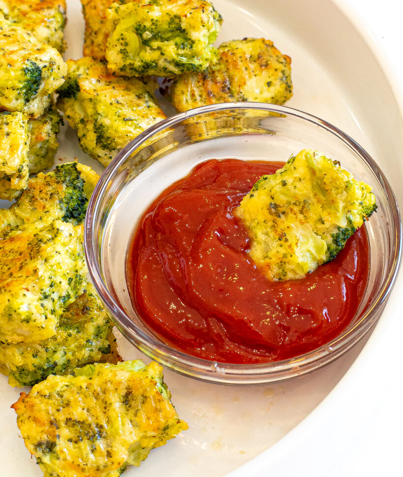 Broccoli cheddar tot being dipped in a small bowl of ketchup. 