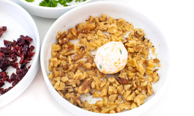 A cheese ball in a bowl with chopped walnuts.