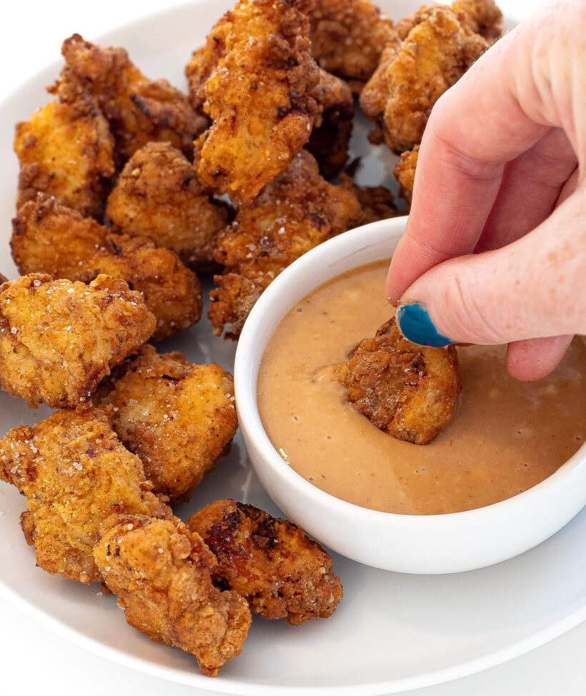 Hand dipping a chicken nugget in a small bowl of sauce with more nuggets next to it.
