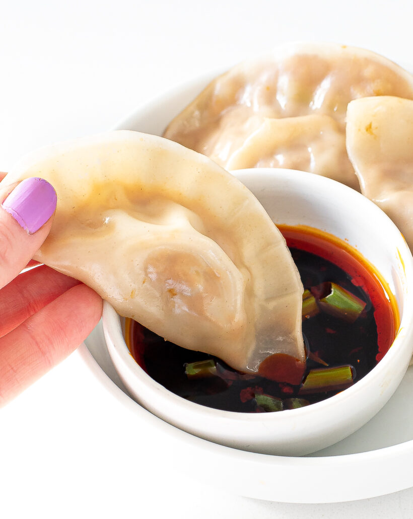 dipping a steamed dumpling in soy sauce and chili oil with green onions on top