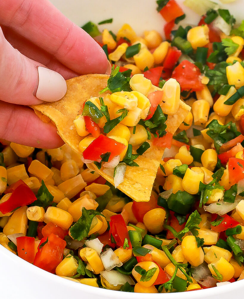 Hand holding a tortilla chip dipped in corn salsa. 