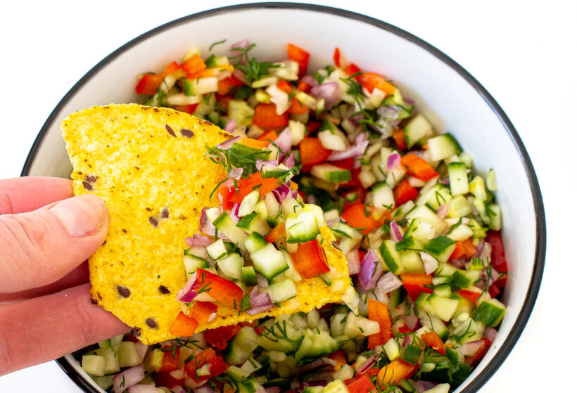 A hand holding a chip with a scoopful of pickle de gallo.