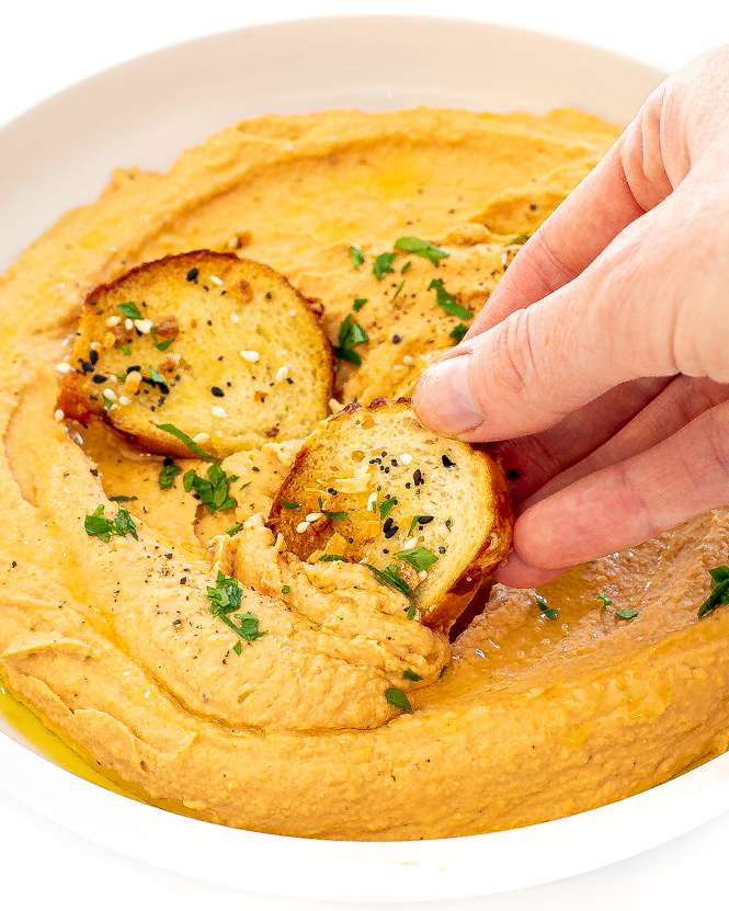 Hand dipping a bagel chip in tomato hummus.