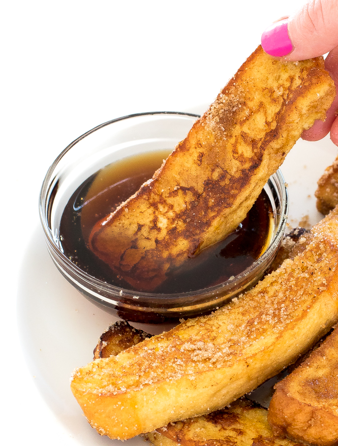 dipping a cinnamon sugar French toast stick into maple syrup on a white plate