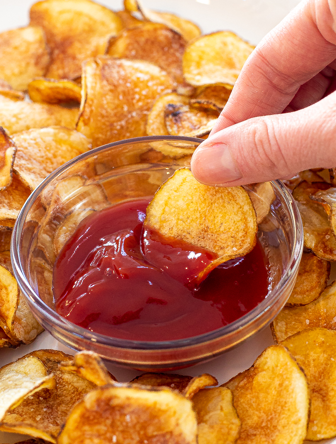 Chip being dipped by a hand into ketchup.