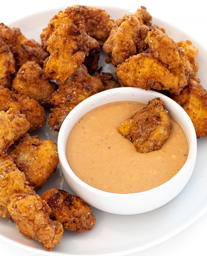 Chick fil a nuggets on a plate with one chicken nugget swimming in the sauce.