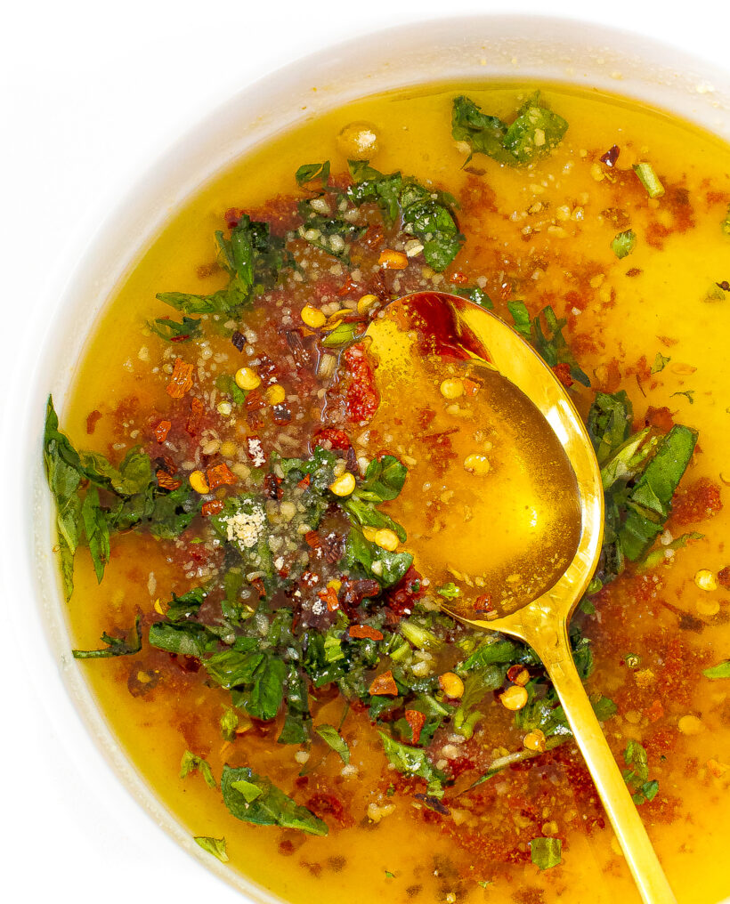 A white bowl filled with dipping oil with a gold spoon in the bowl.