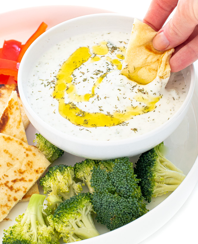 Hand dipping pita into a bowl of sauce.