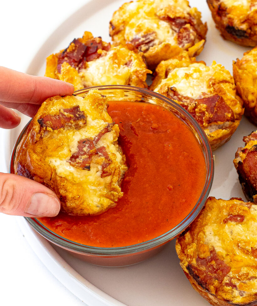 author scooping pizza muffin into a small bowl of marinara sauce