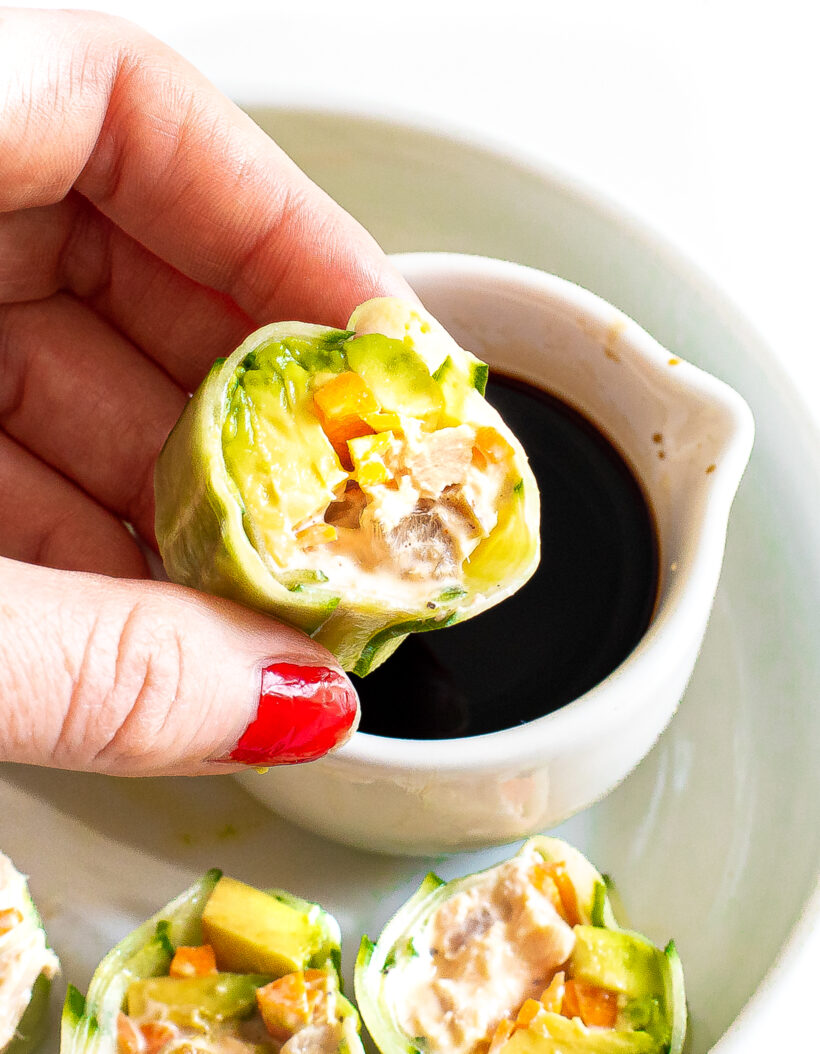 Hand holding a piece of cucumber tuna sushi and dipping it in soy sauce.