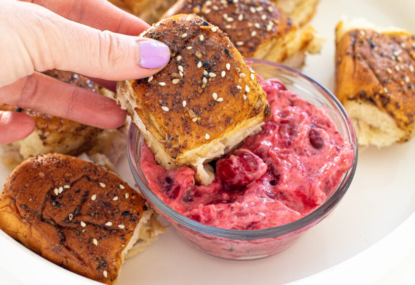 Hand dipping a turkey cheese slider into cranberry mayo.