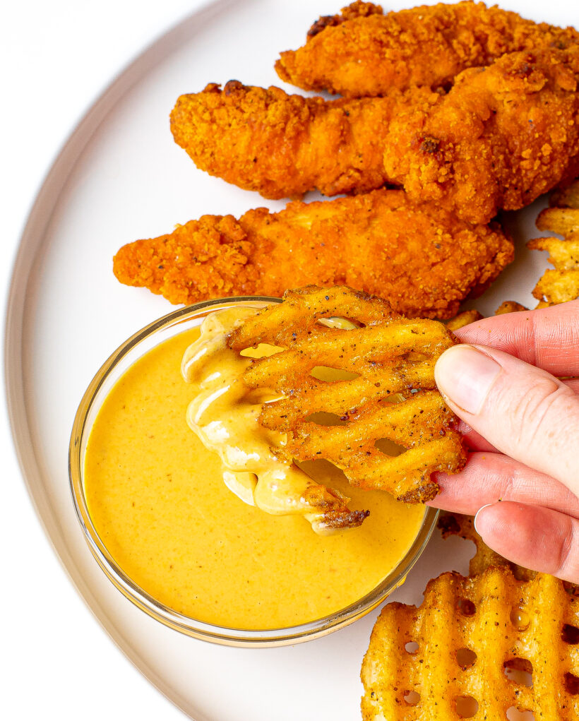 Hand dipping waffle fry into homemade Chick Fil A Sauce.
