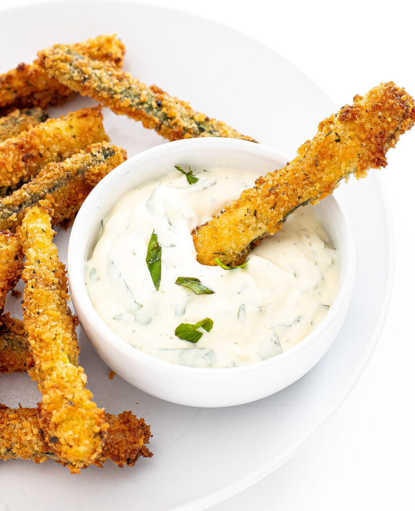 Zucchini fries on a plate with one fry being dipped into a sauce.