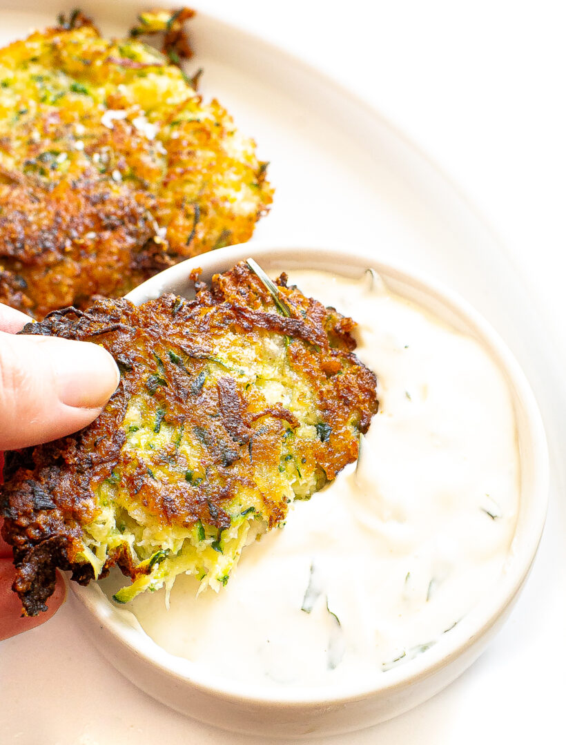 Hand dipping a zucchini fritter into dip.