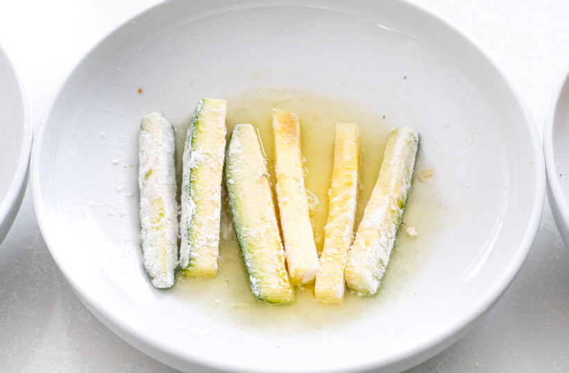Zucchini spears being dipped into egg white.