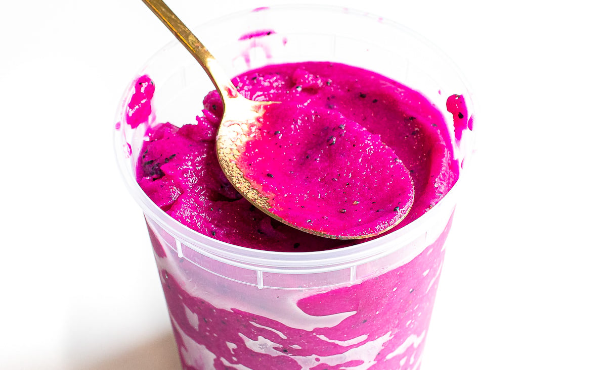 Scooping dragon fruit water ice out of a plastic container with a spoon.