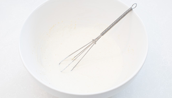 Mayonnaise and sour cream being whisked in a white bowl with other ingredients. 