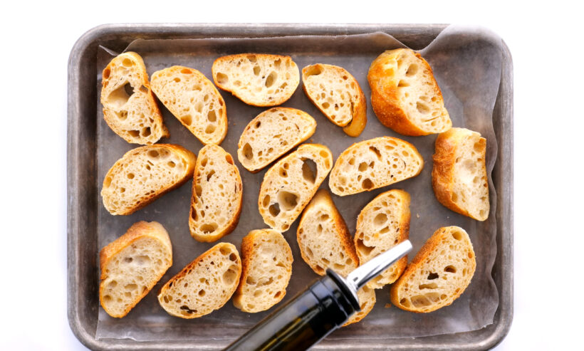 drizzling olive oil on a baguette on a baking sheet