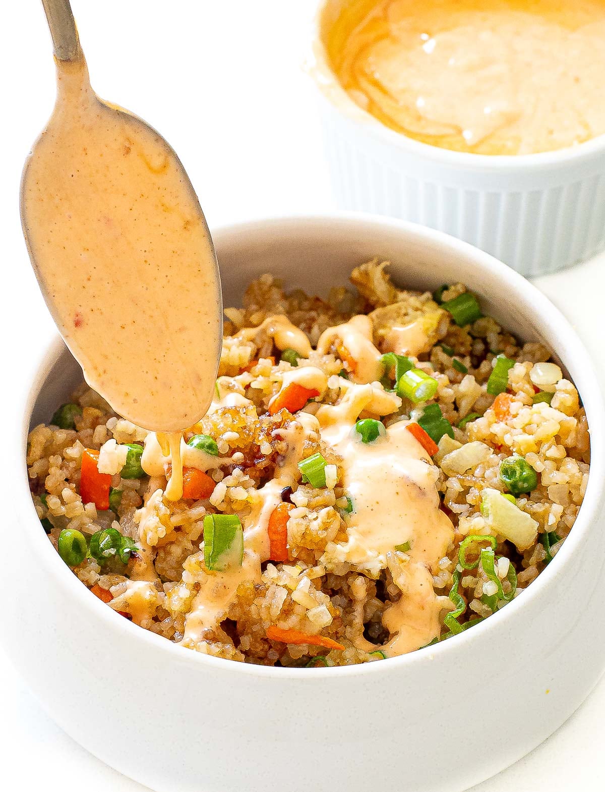 drizzling homemade bang bang sauce on top of air fryer fried rice