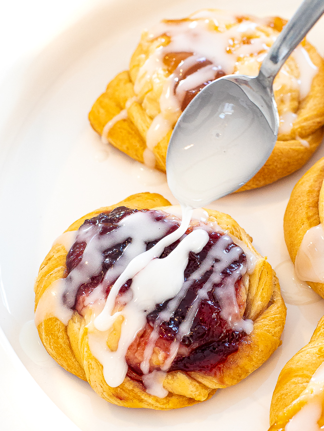 Cream cheese crescent danish with spoon drizzling glaze on the top. 