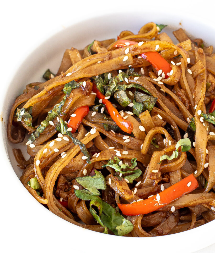 Drunken noodles served in a white bowl with sesame seeds on top. 