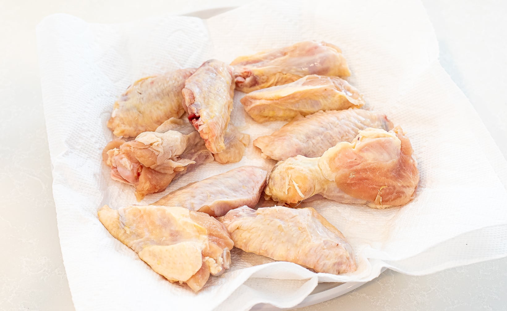 Raw chicken wings on paper towels on a plate.