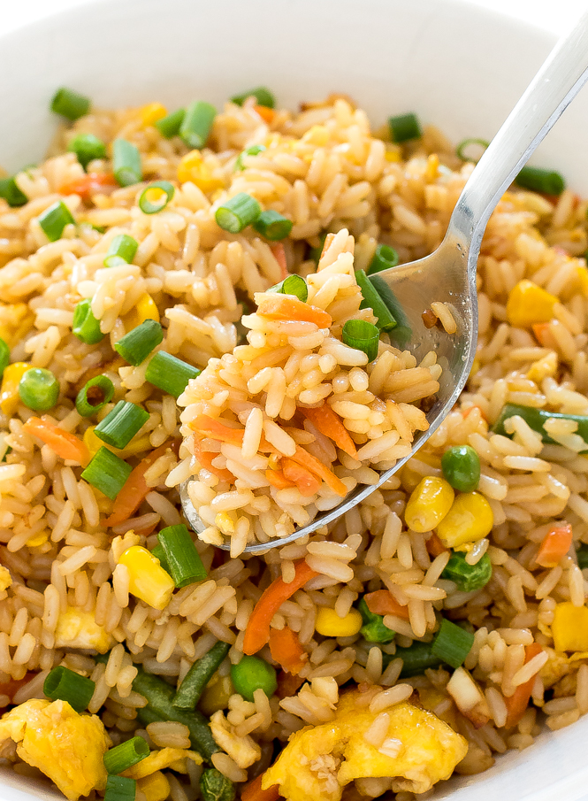 Vegetable rice in a white bowl with a spoon lifting rice out.