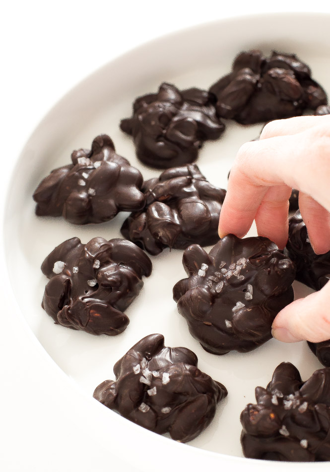 hand picking up a dark chocolate almond cluster, several clusters placed on a white plate