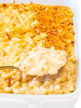 A spoonful of baked macaroni and cheese being lifted from a white ceramic casserole dish.